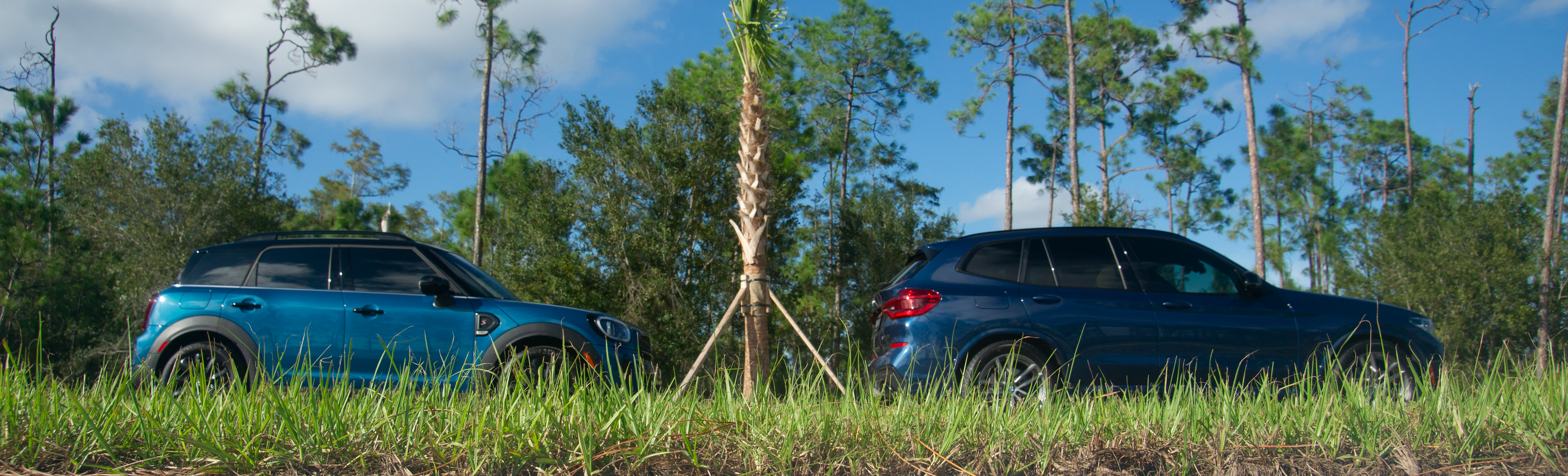 Blue Mini Cooper Countryman S and BMW X3 M40i behind grass